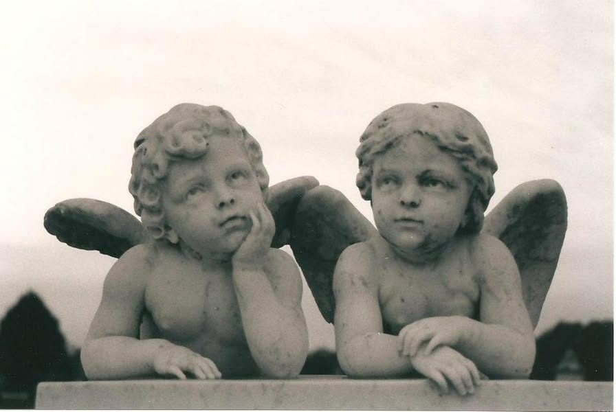 Two winged marble cherubs leaning on the edge of a monument