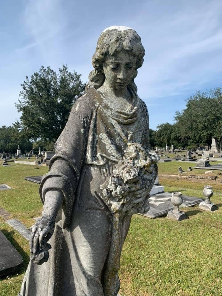 Weathered stone figure of a young woman carrying a bouquet of roses